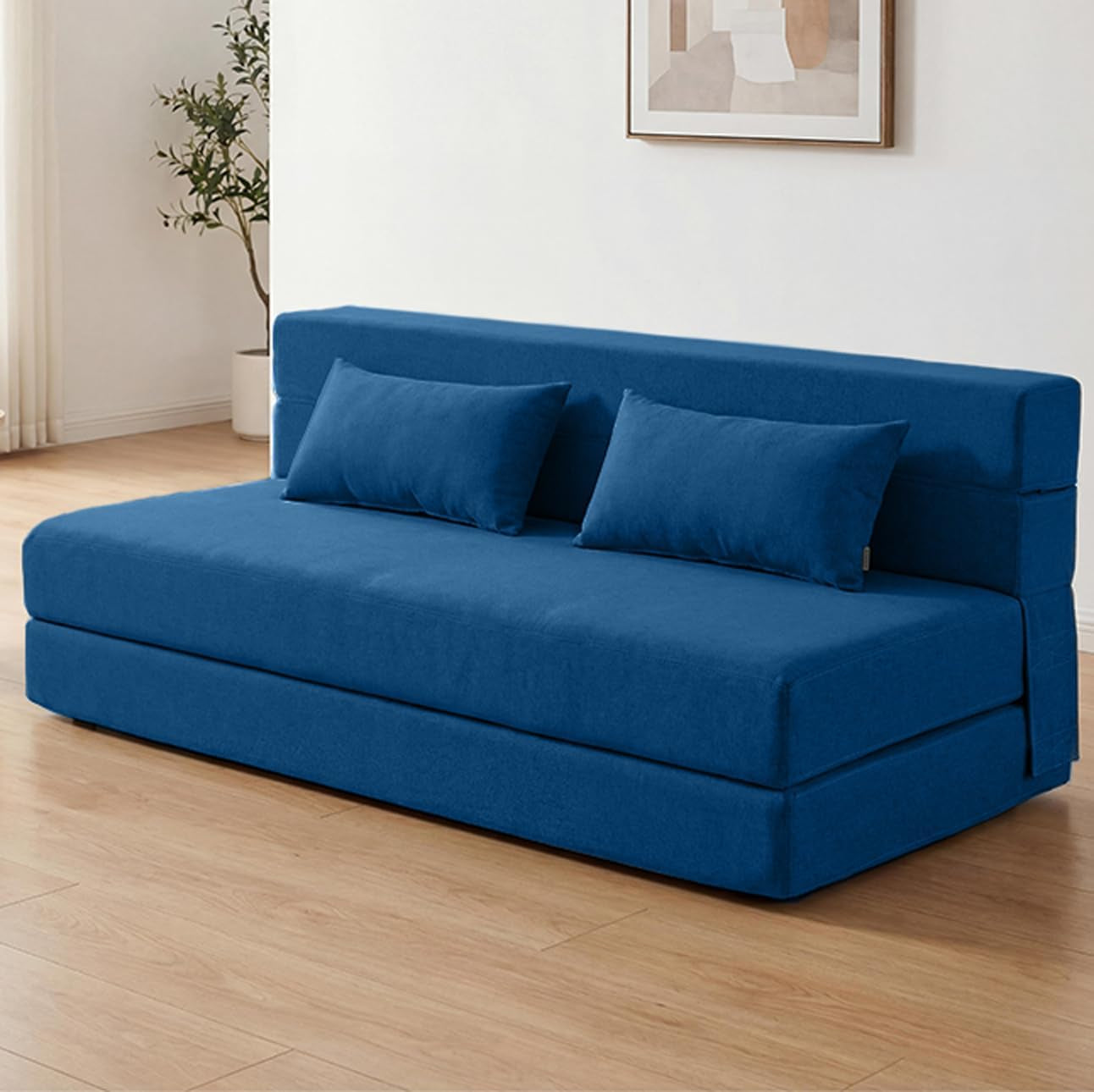Blue sofa bed in a living room setting with two pillows and wall art above.