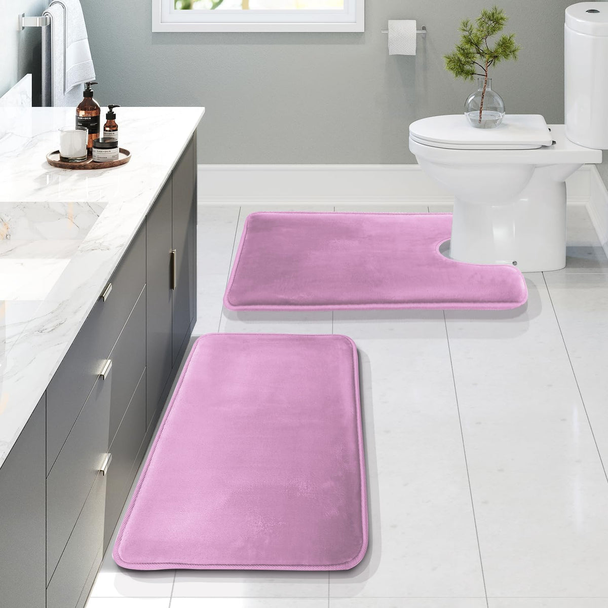 Angled bathroom view showing a pink U-shaped contour mat at the toilet and two matching rectangular rugs by the vanity.