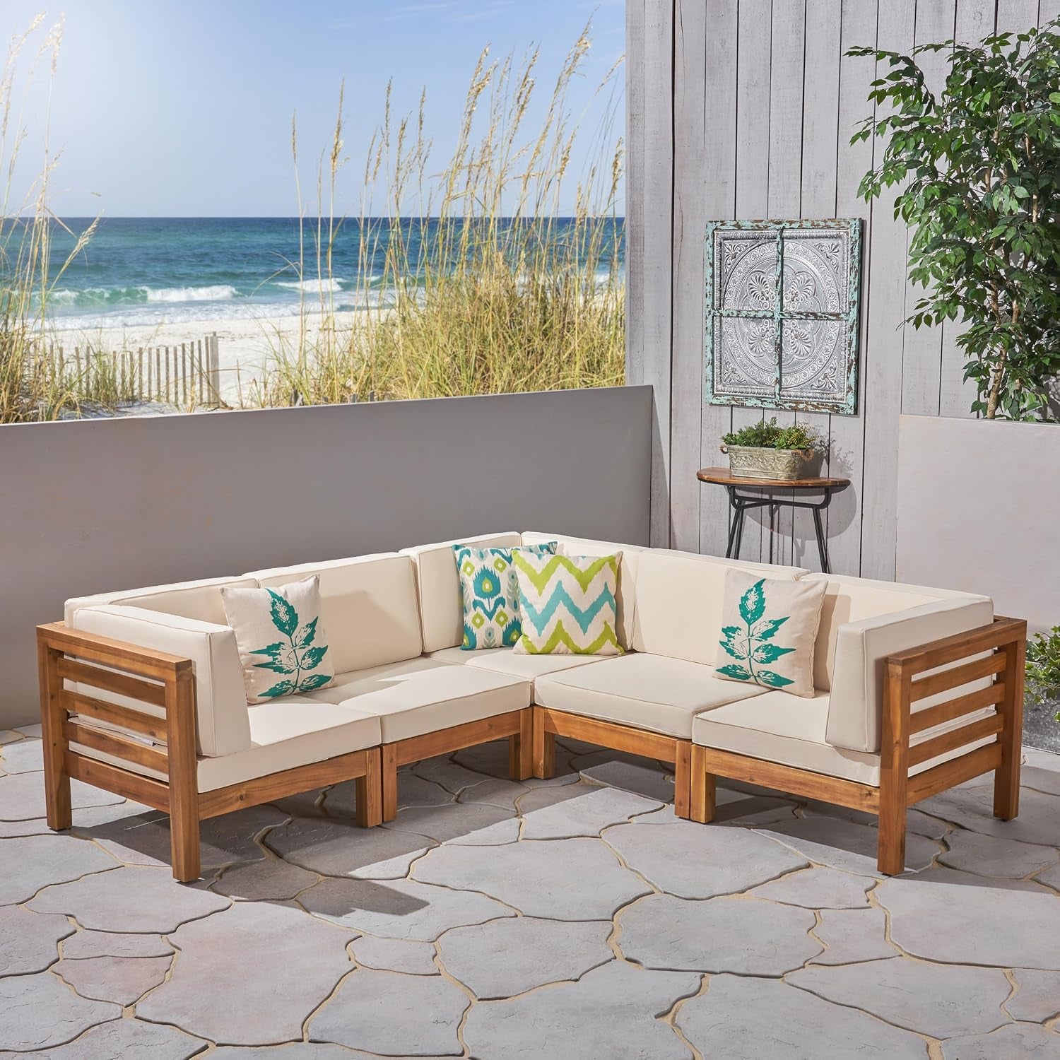 5-seat modular outdoor sectional with beige cushions and decorative pillows on a stone patio by the ocean