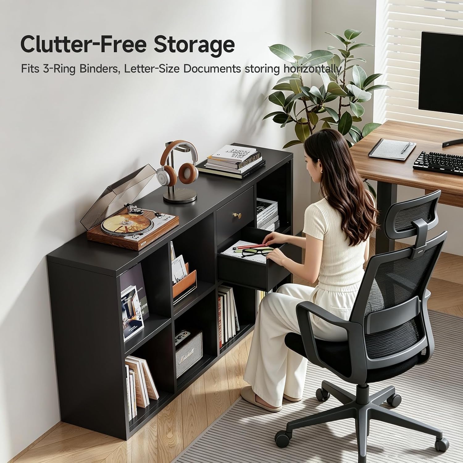 Black 8-cube shelf beside a desk with a person accessing a storage drawer and letter-size binders visible in cubbies.