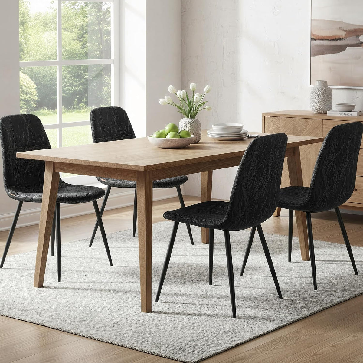 Four black chairs paired with a light wood table and vase of tulips in a bright dining room