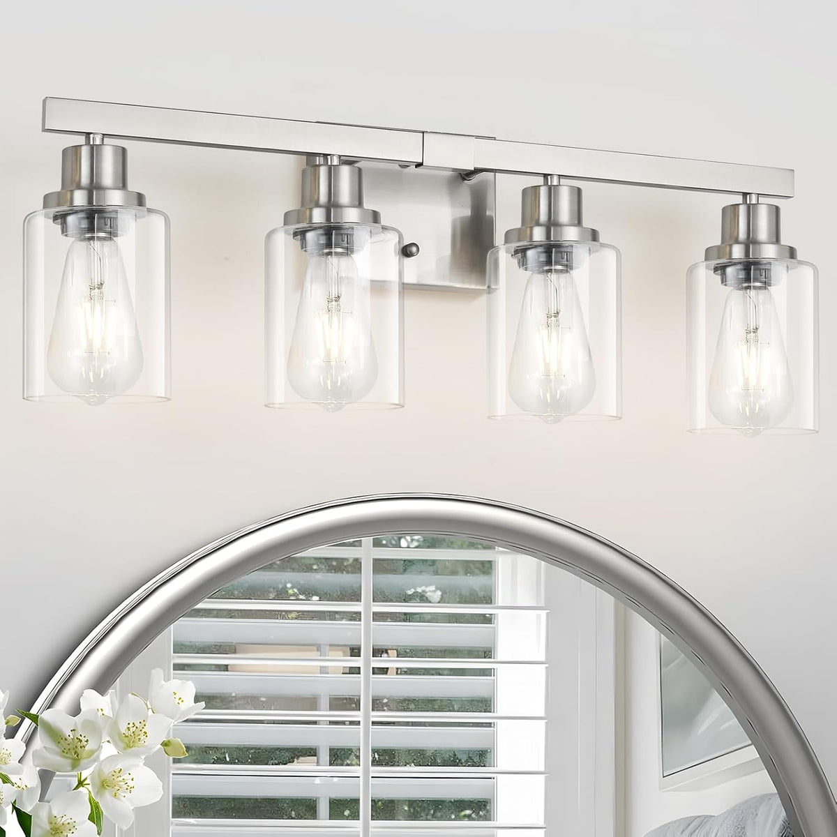 Front-facing close-up of a four-light brushed nickel vanity fixture showing clear glass shades and exposed bulbs.