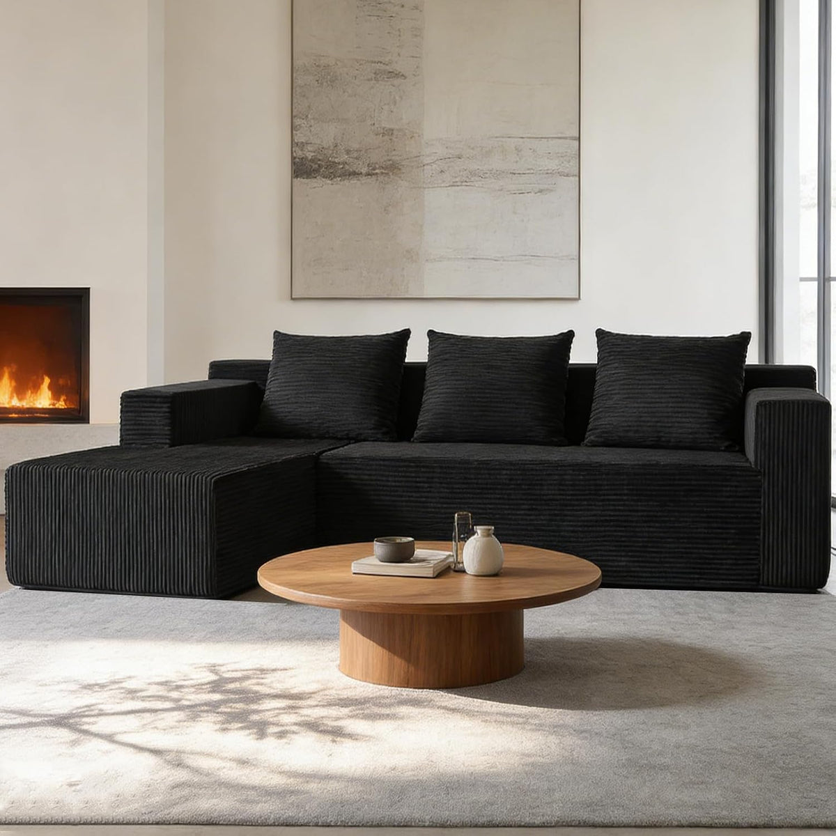 Black corduroy-texture sectional with three back pillows and low round wooden coffee table in a modern room.