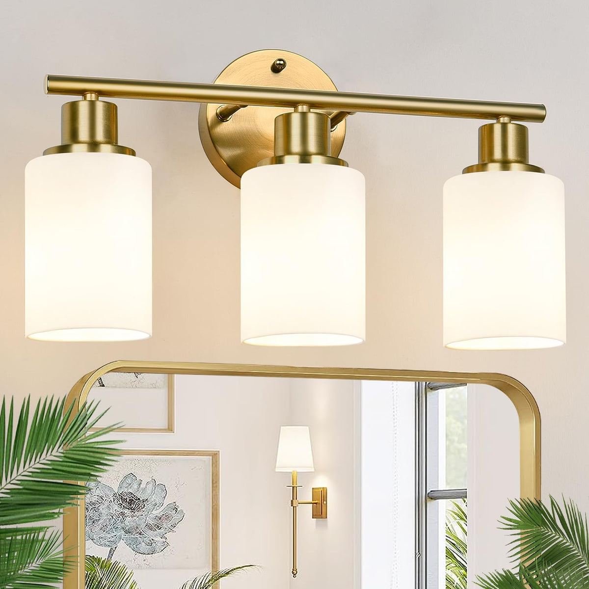 Close-up of a three-light brass vanity fixture with three frosted cylindrical glass shades over a mirror.