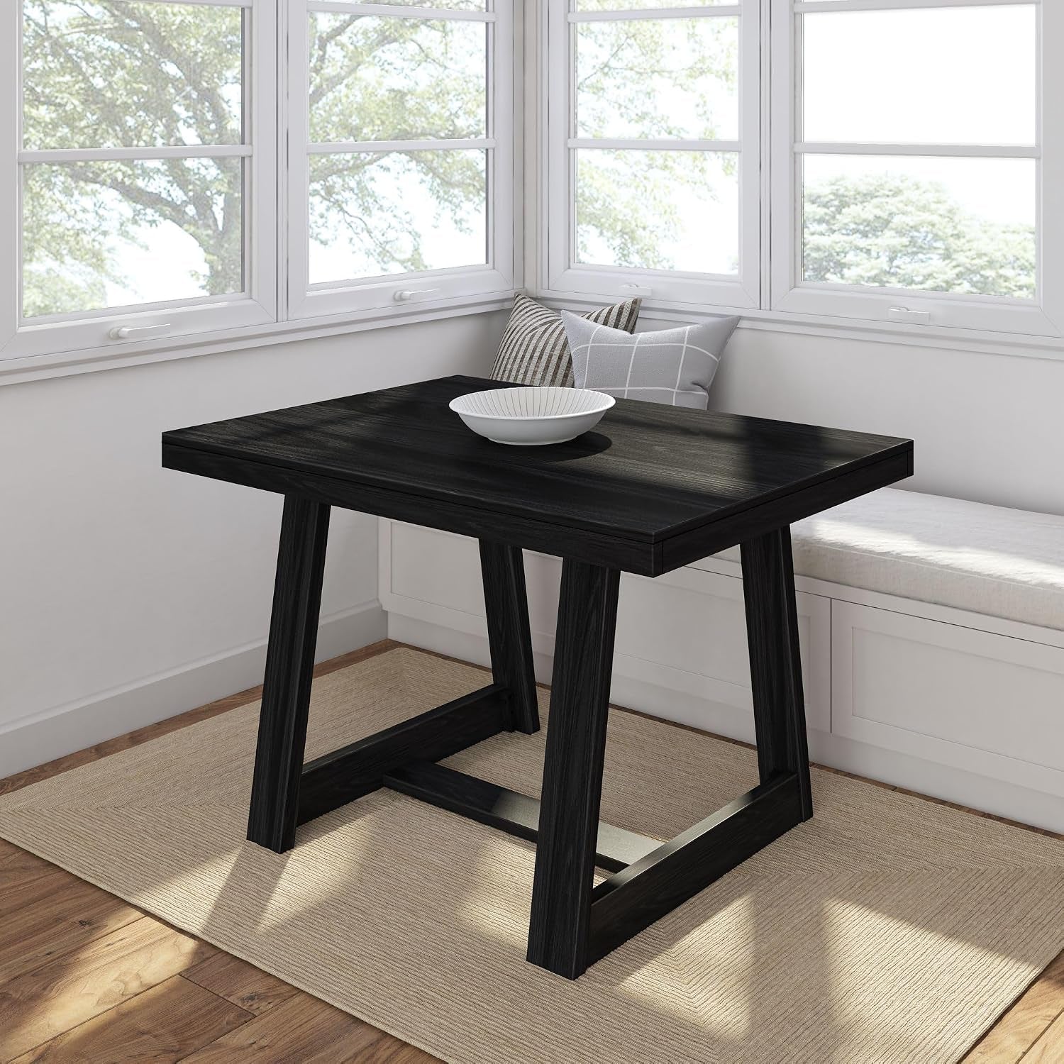 Square dining table with trestle-style legs in a dark wood finish in a bright windowed nook