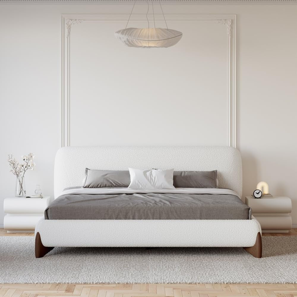 White boucle upholstered low platform bed front view with rounded white nightstands in a neutral bedroom