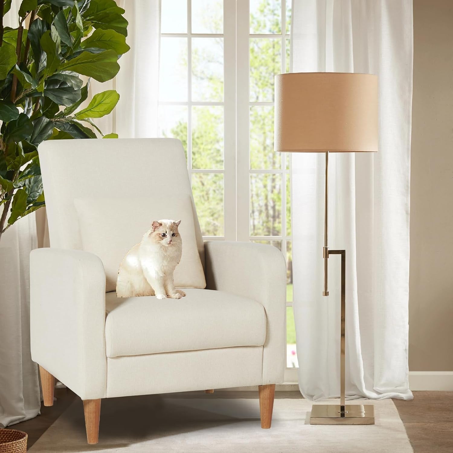 Cream upholstered accent chair with wood legs and a cat sitting on the seat next to a floor lamp