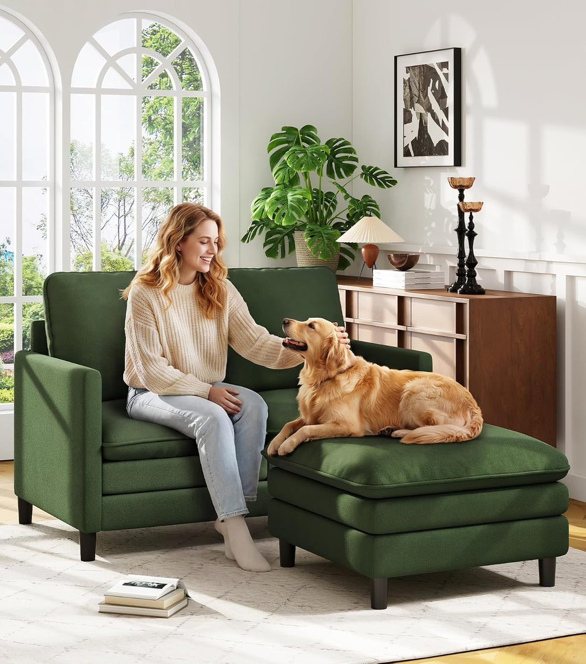 Woman sitting on a green loveseat petting a golden retriever sprawled on the matching ottoman in a bright living room.