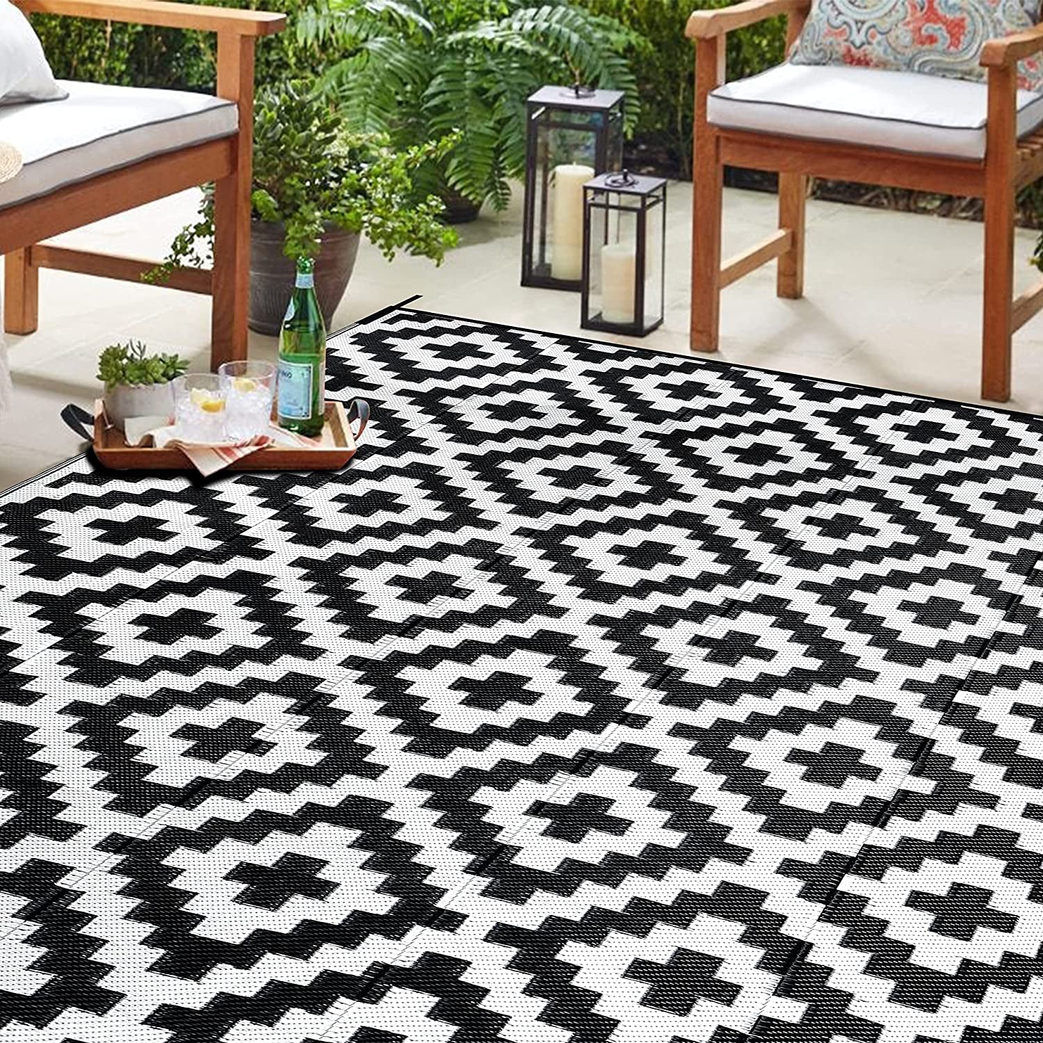 Close-up patio view of a black-and-white geometric outdoor rug under wooden chairs and a tray with drinks.