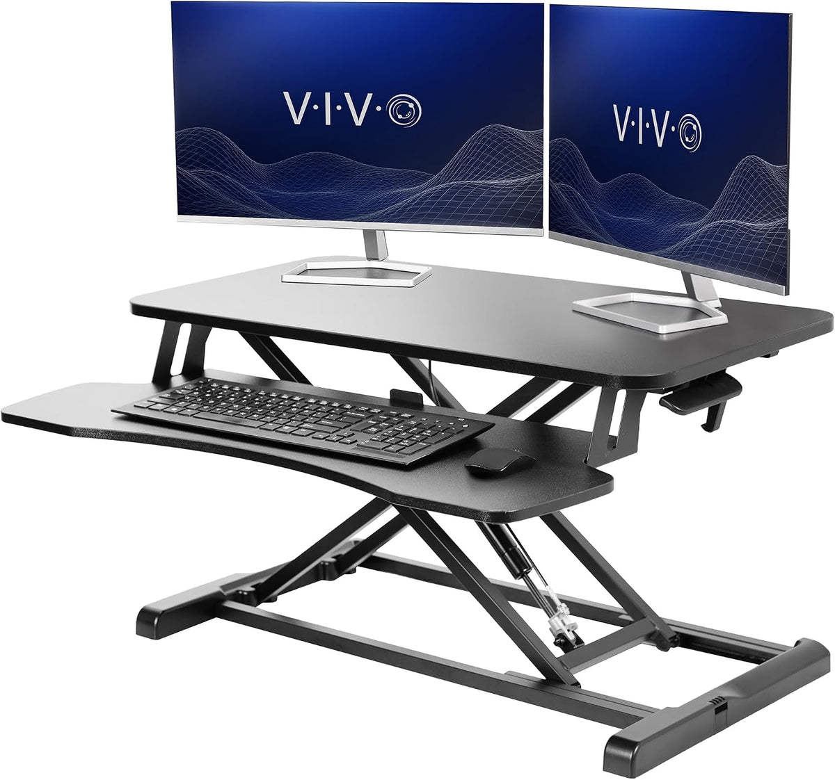 Black standing desk converter with scissor lift, keyboard tray and two monitors on a tabletop.