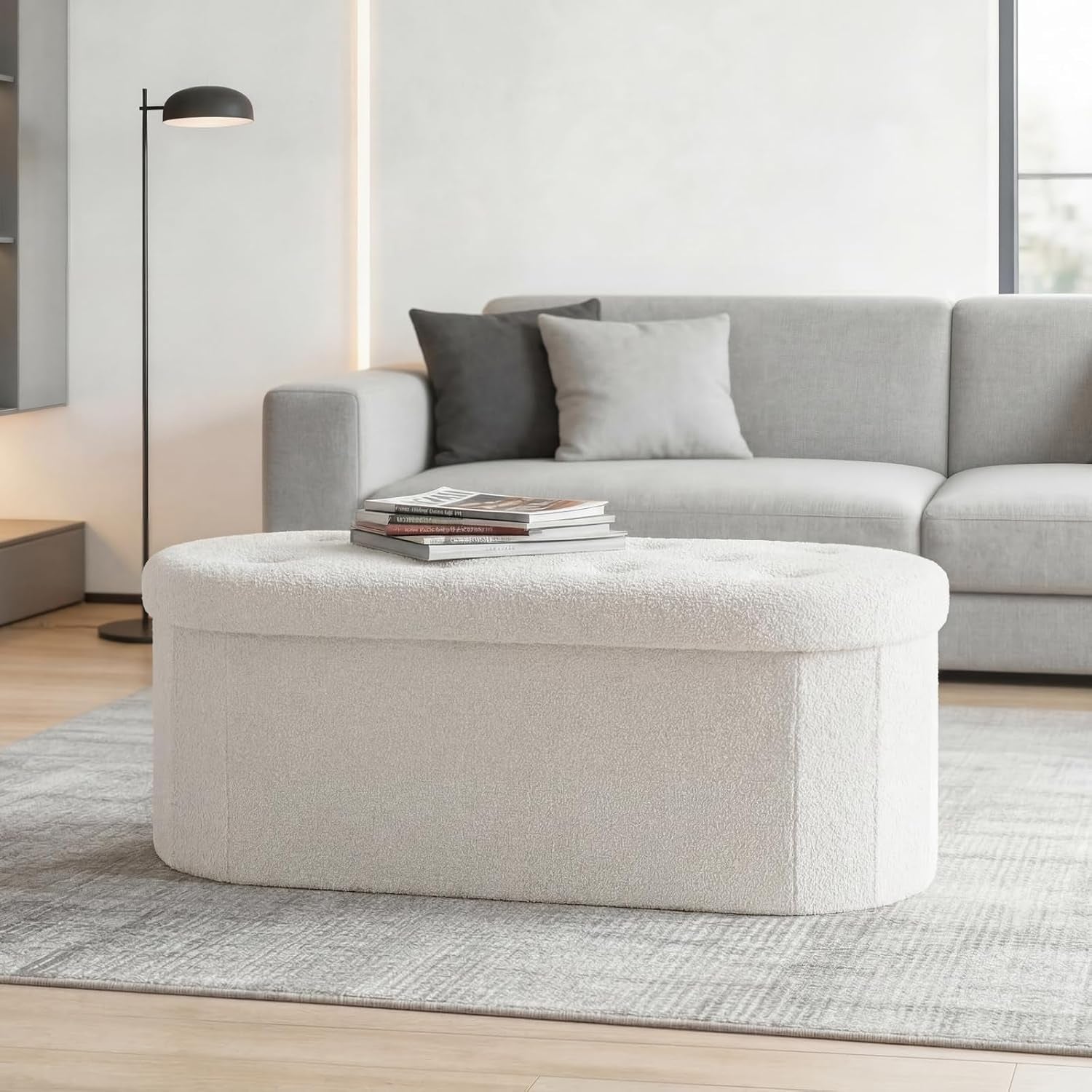 White oval storage ottoman with tufted top angled front view in a living room
