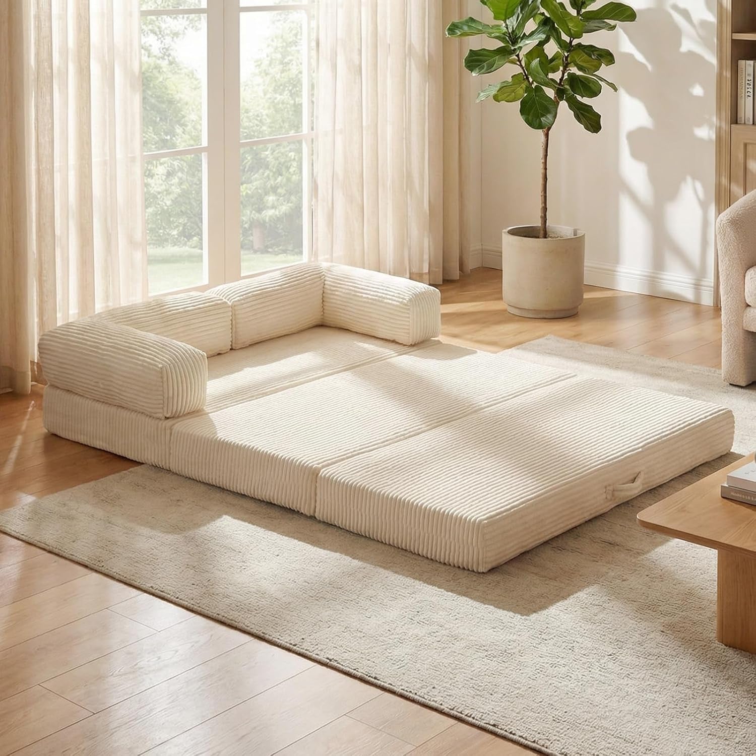 Low-profile tri-fold mattress laid flat on a rug in a sunlit living room with removable padded armrests.
