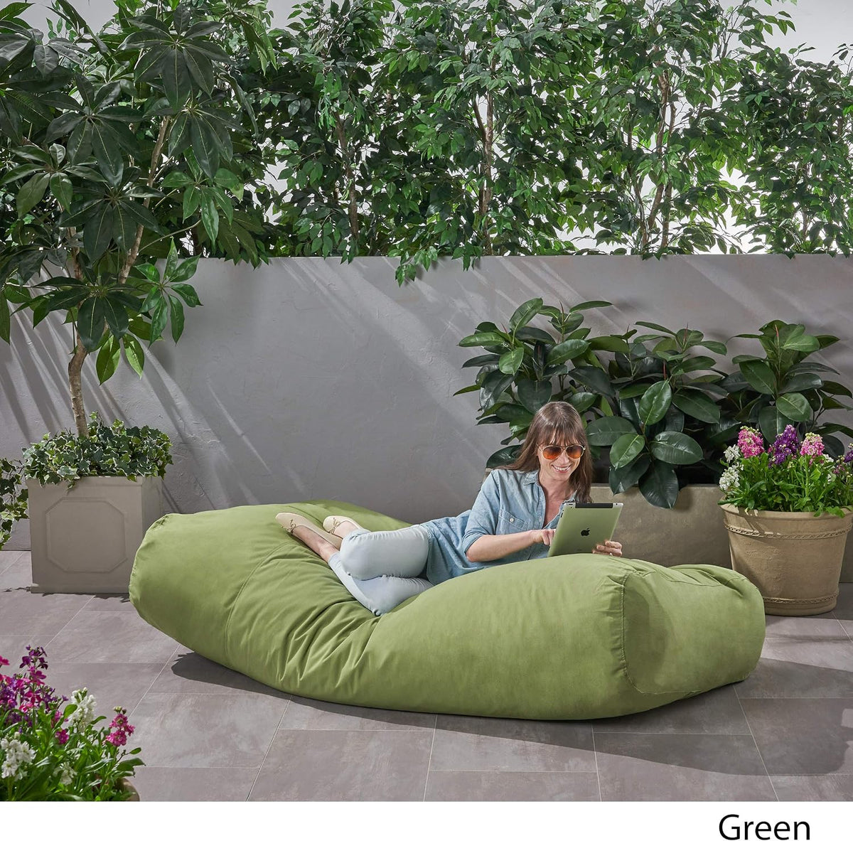 Lifestyle top-angle view of a person using the green rectangular lounger outdoors near plants