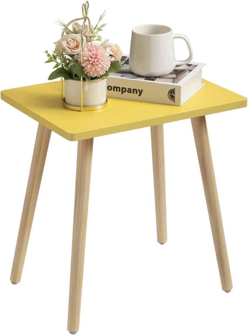 Yellow square side table with natural wood legs holding a mug, book and small floral arrangement