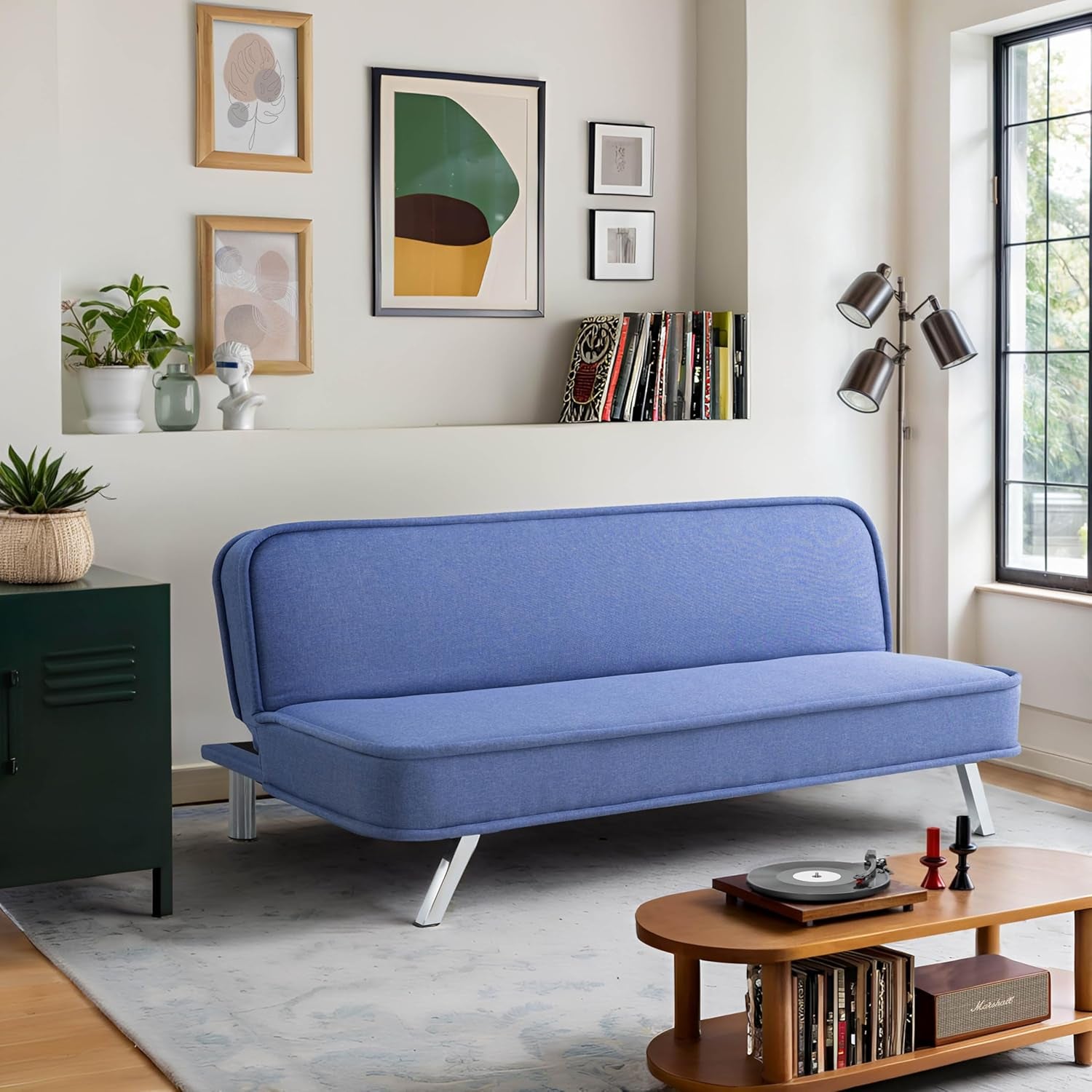 Light blue convertible futon sofa with slanted metal legs in a styled sitting area by a window.
