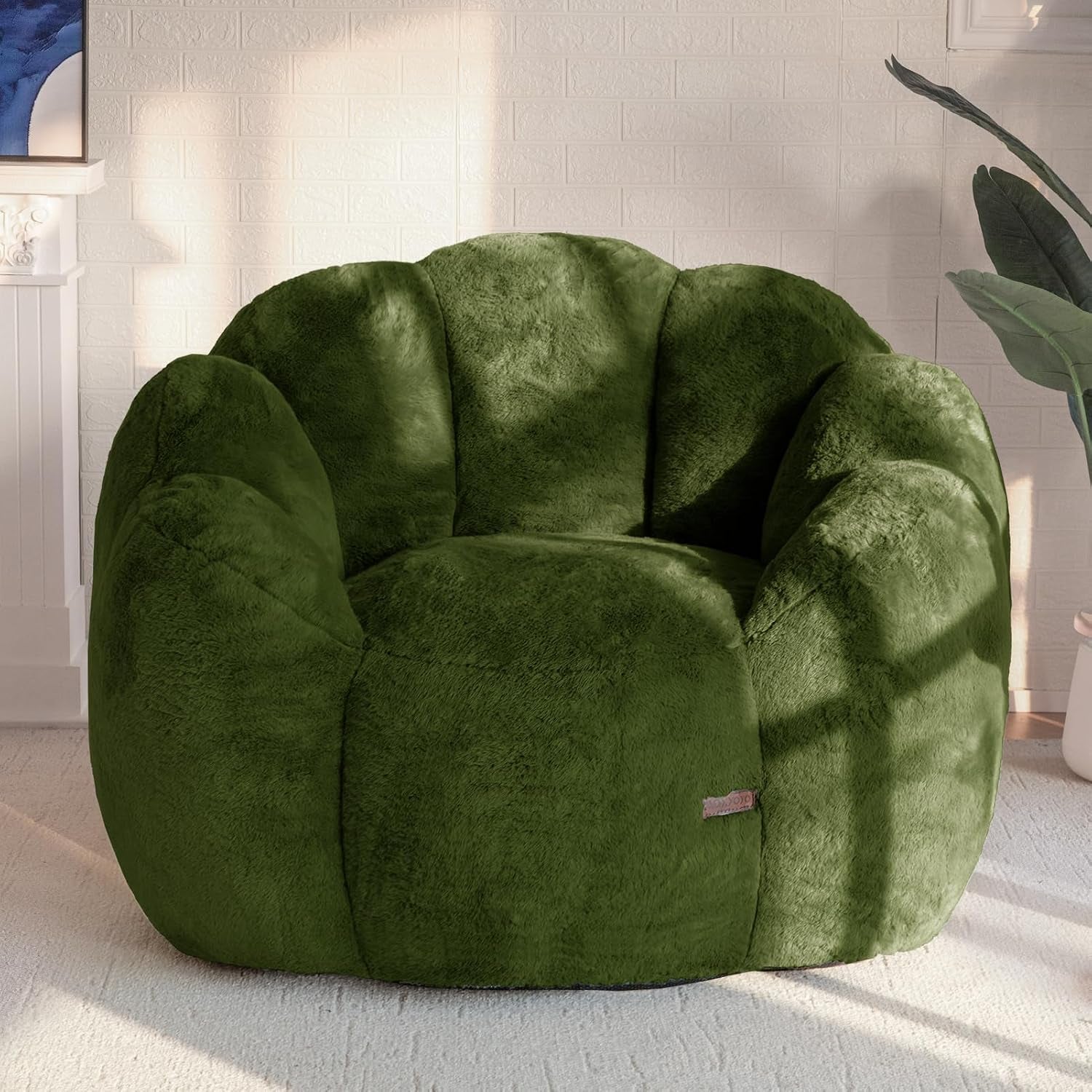 Plush floral-shaped bean bag chair in deep green placed on a light rug against a white brick wall.