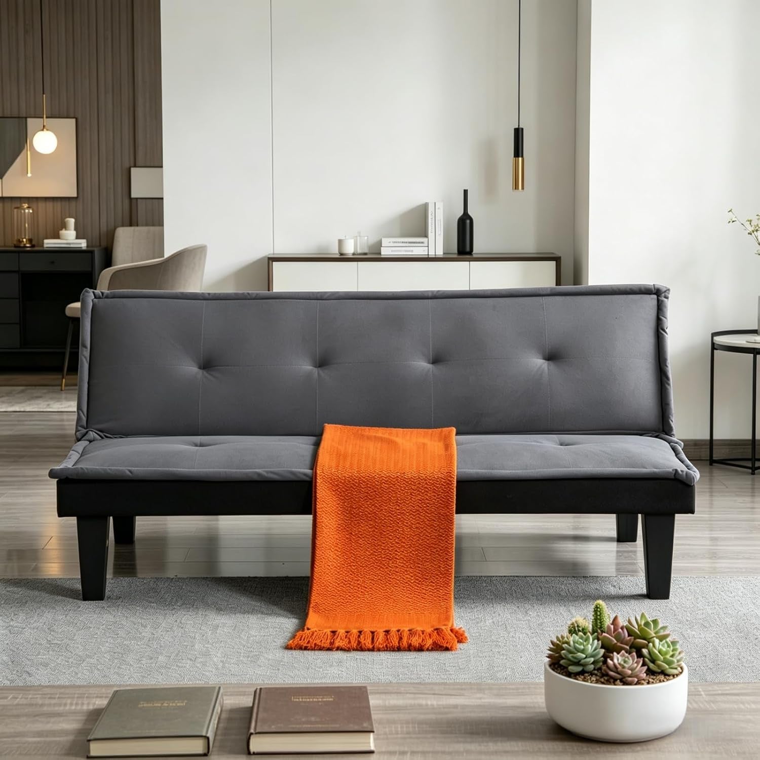 Dark gray futon set as a bench with an orange throw running down the center and succulents on the coffee table.