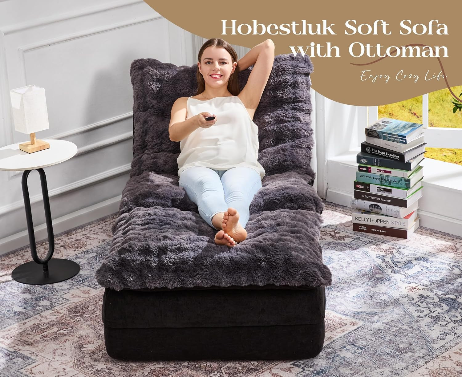 Front view of the floor sofa with ottoman; a woman lies back holding a remote, books stacked by the window.