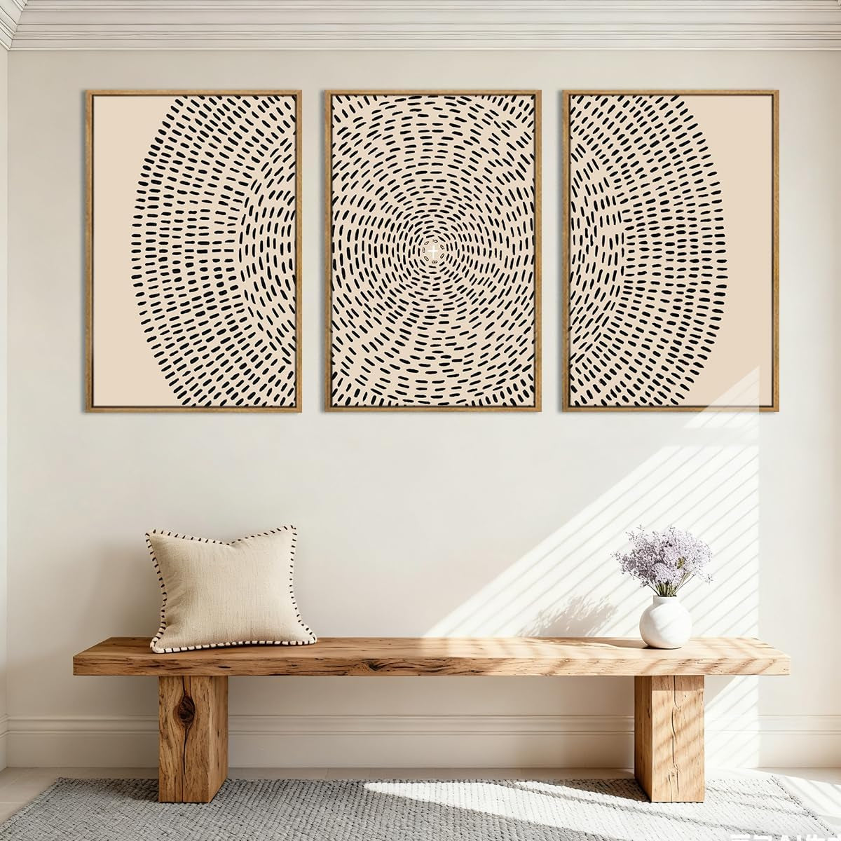 Three beige canvas prints with black dot-line radial design in wood frames over a bench in an entryway