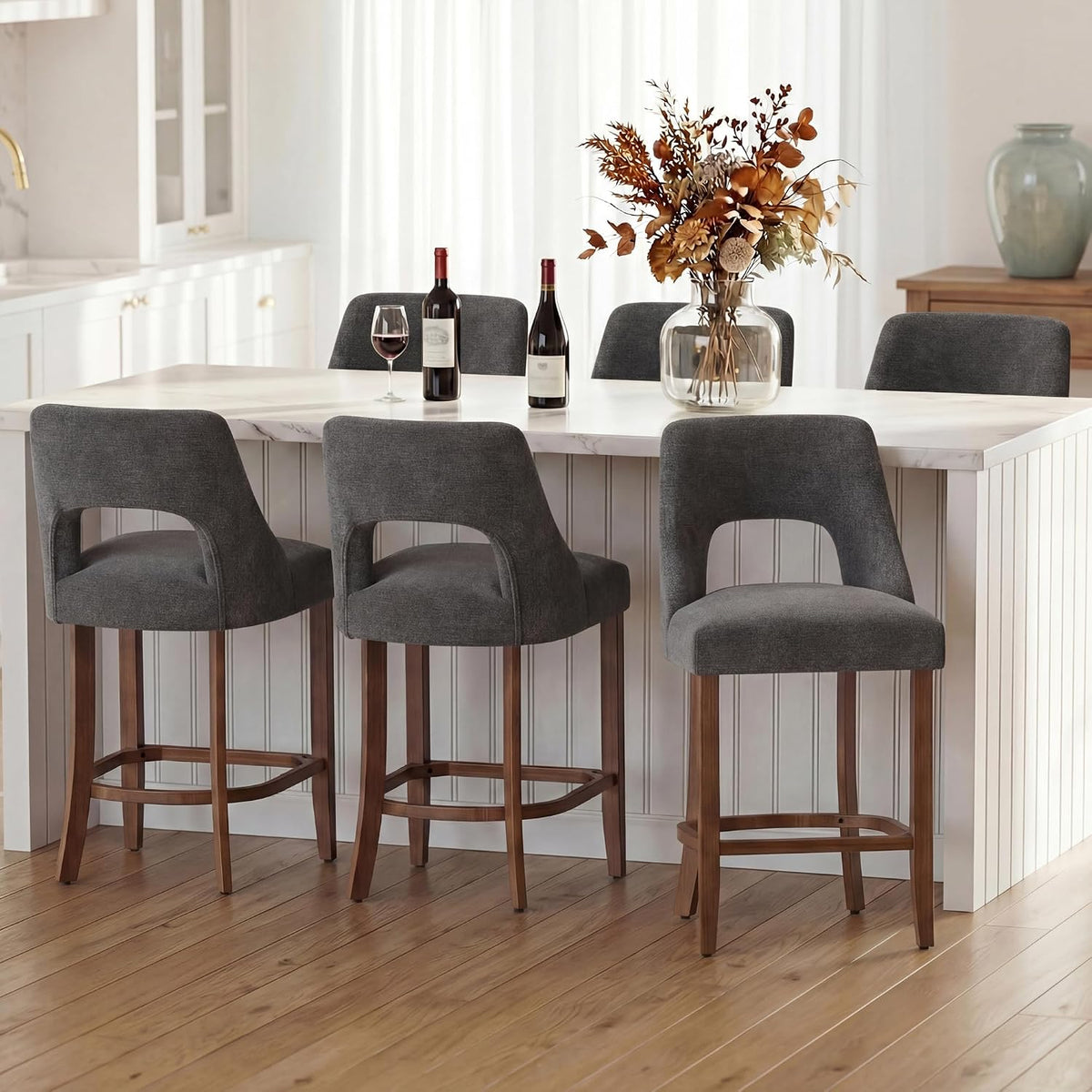 Four dark gray upholstered counter stools lined along a white kitchen island with wood floors.