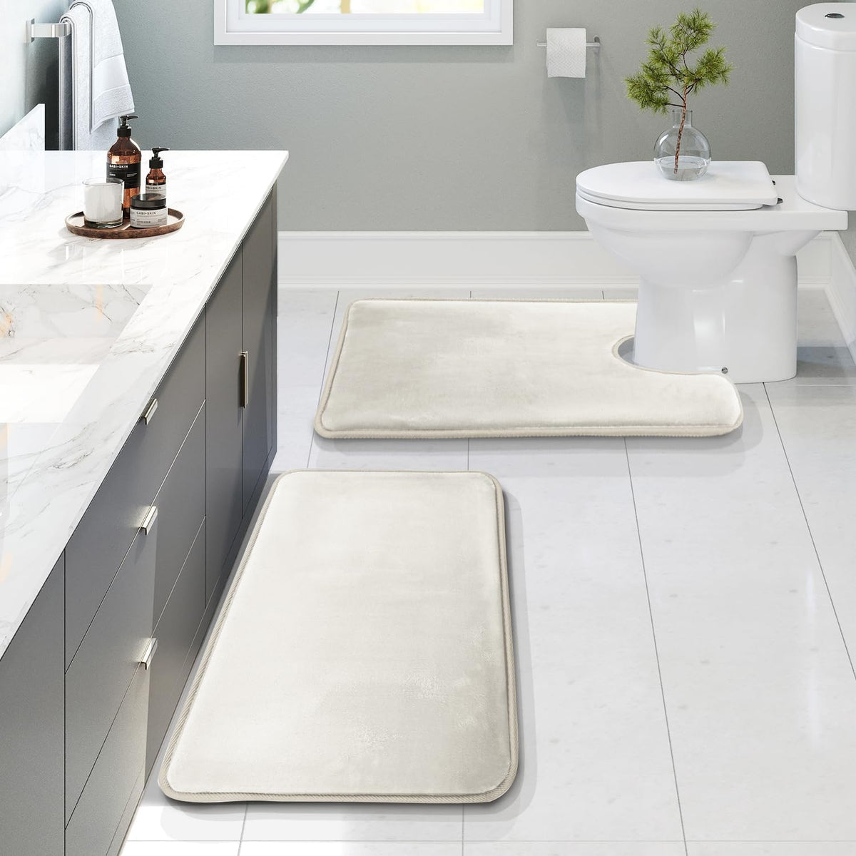Angled bathroom scene showing three ivory memory-foam rugs, including a U-shaped contour mat positioned at the toilet.