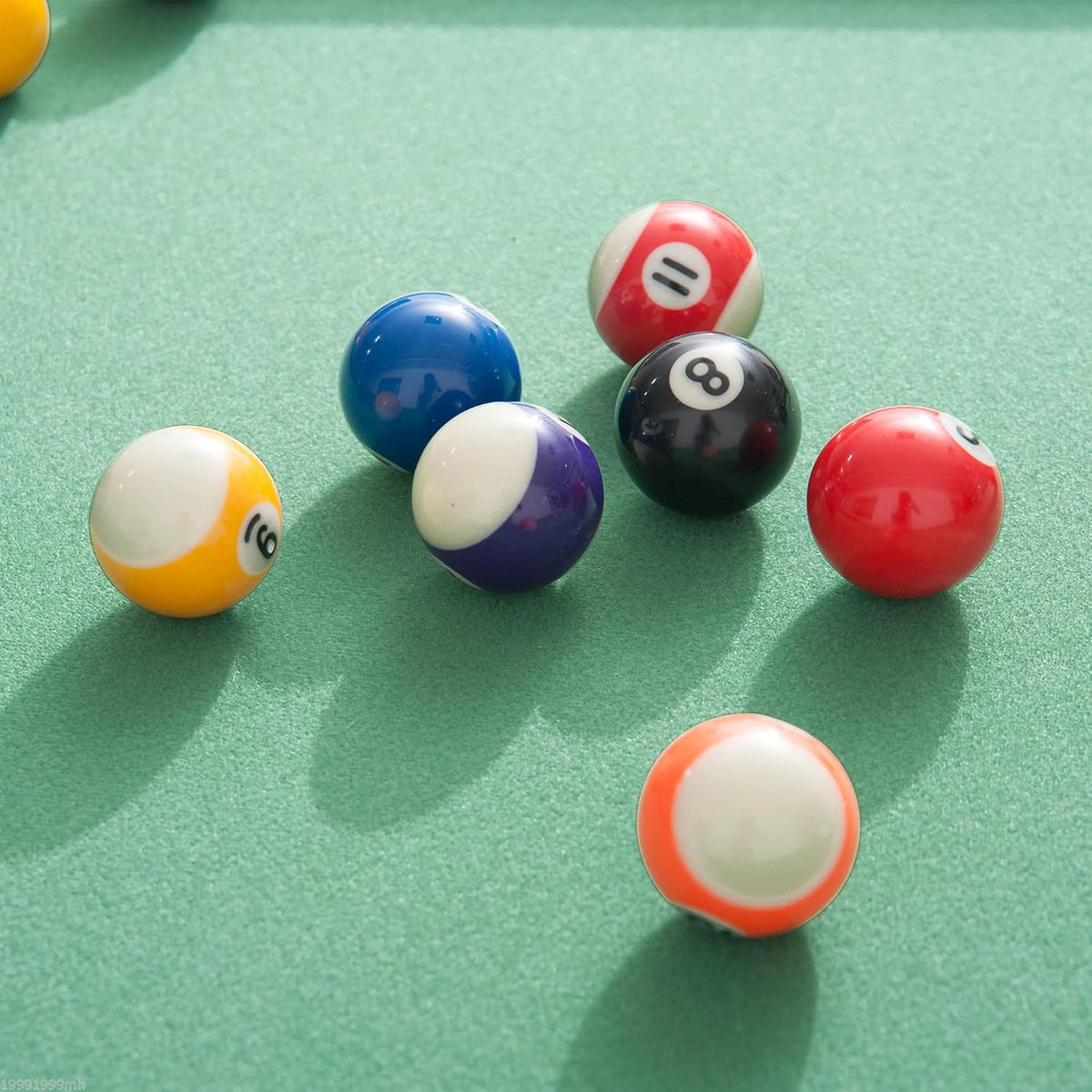 Close-up of assorted colorful pool balls scattered on a green felt surface with soft shadows.