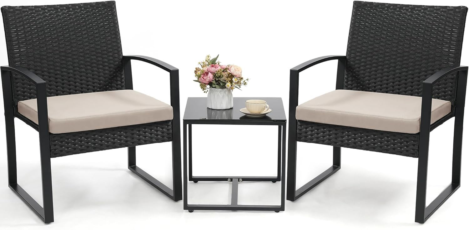 Two black-rattan armchairs with beige seat cushions and a small black glass-top side table with a cup and flowers
