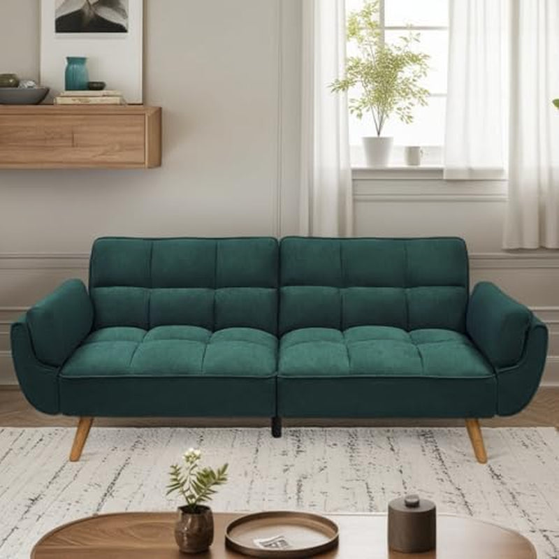 Deep teal velvet futon sofa placed against a windowed wall with a round wood coffee table.