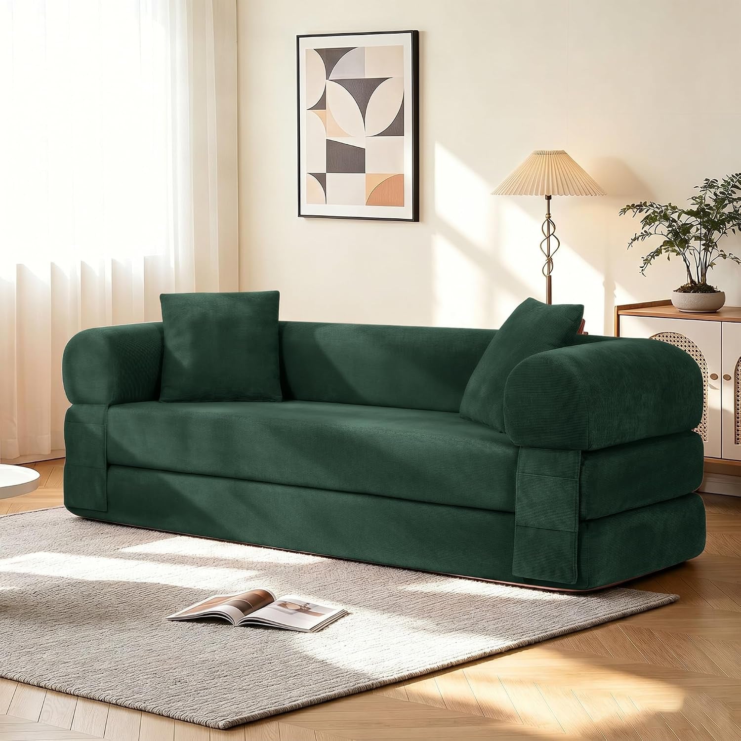 Deep forest green corduroy convertible sofa with two matching pillows in a sunlit corner of a living room.