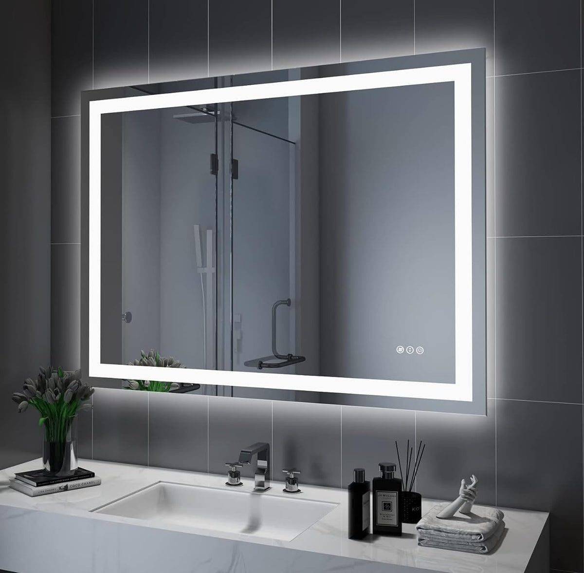 Angled view of illuminated rectangular mirror reflecting a shower, mounted on gray tiled wall above sink.