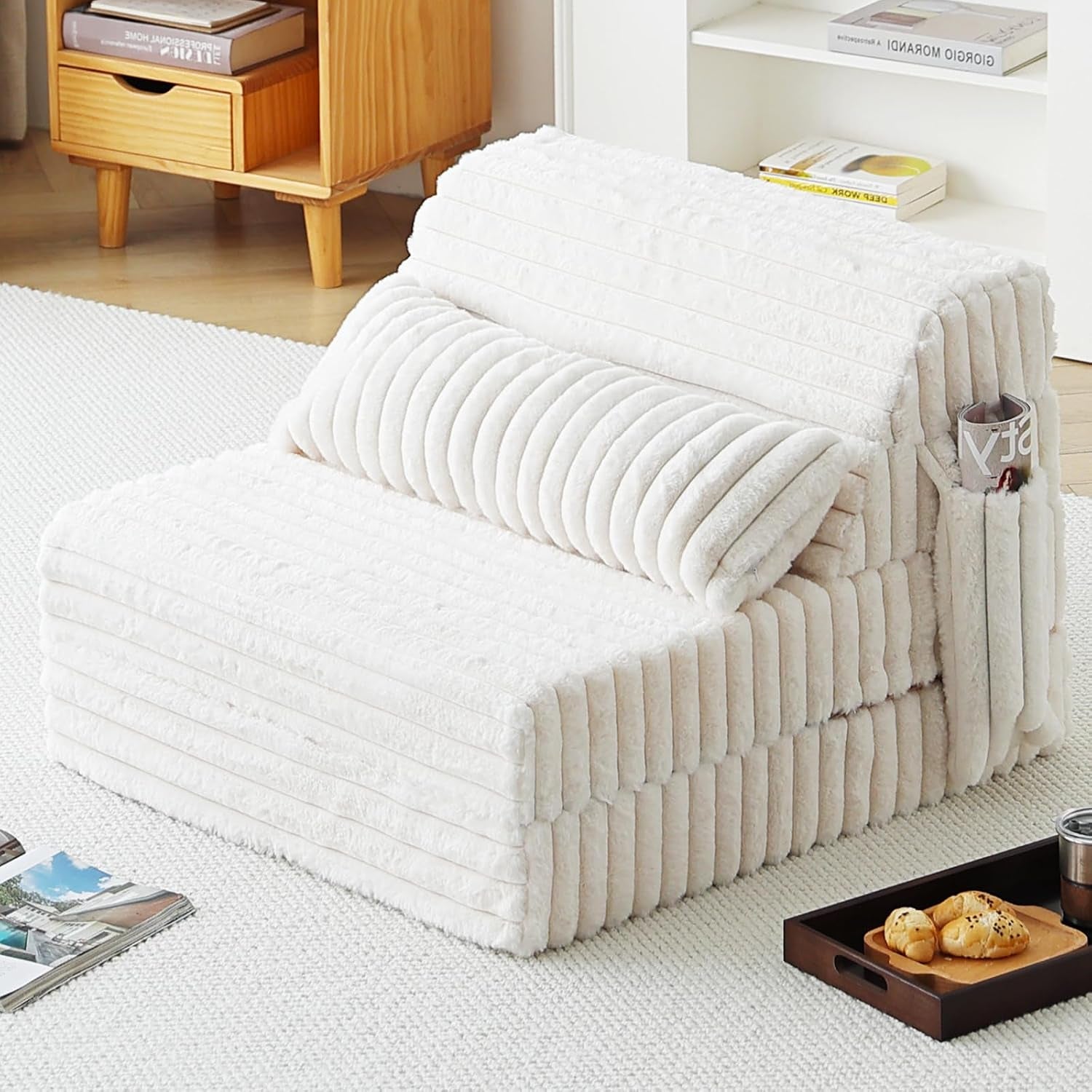 Cream folding floor sofa with lumbar pillow and side pocket holding a magazine