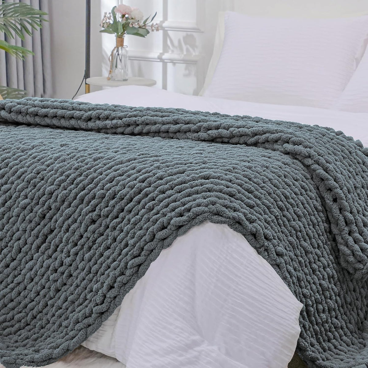 Muted gray chunky knit throw spread across the end of a bed, showing the thick braided texture.