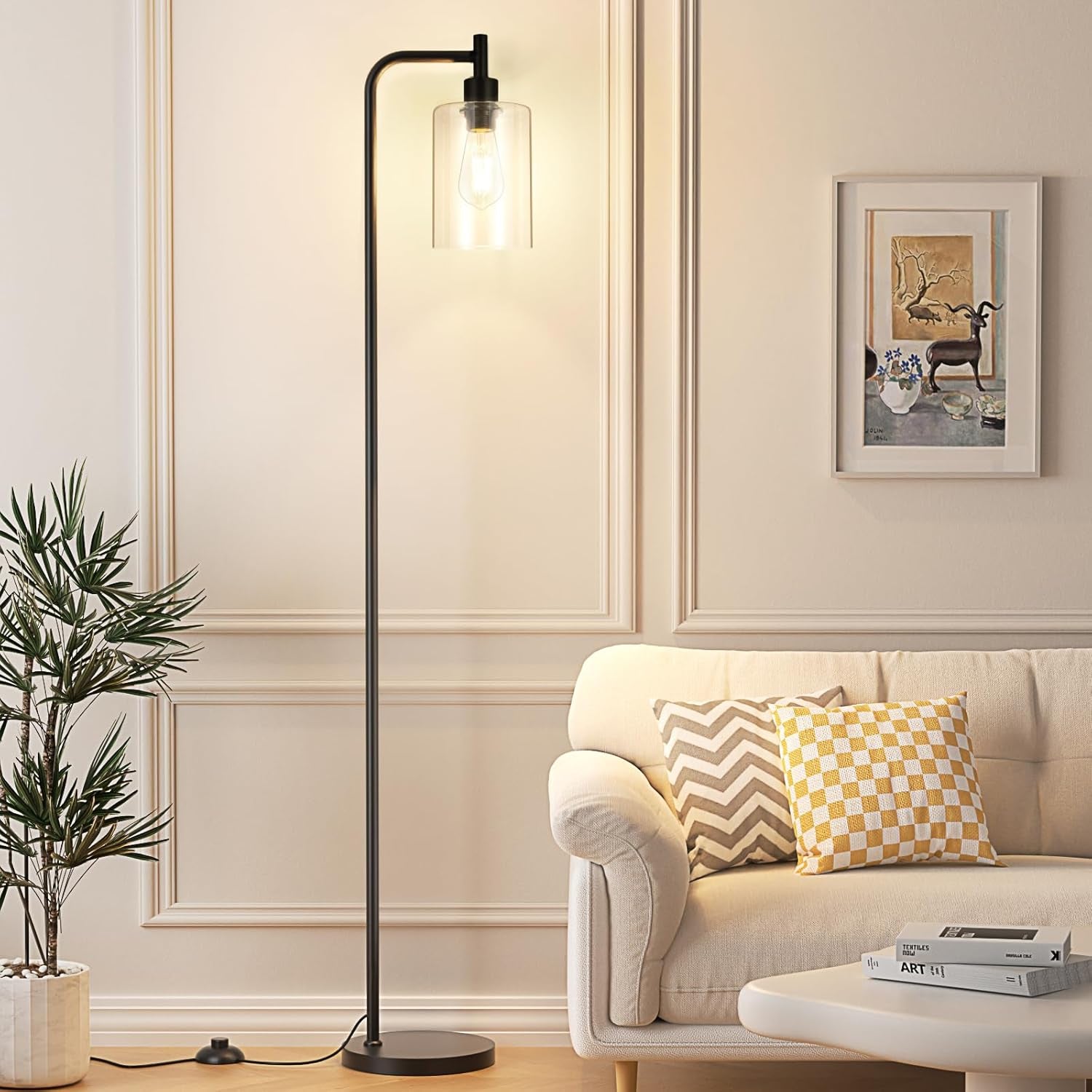 Black floor lamp with clear cylindrical glass shade beside a sofa, angled front view