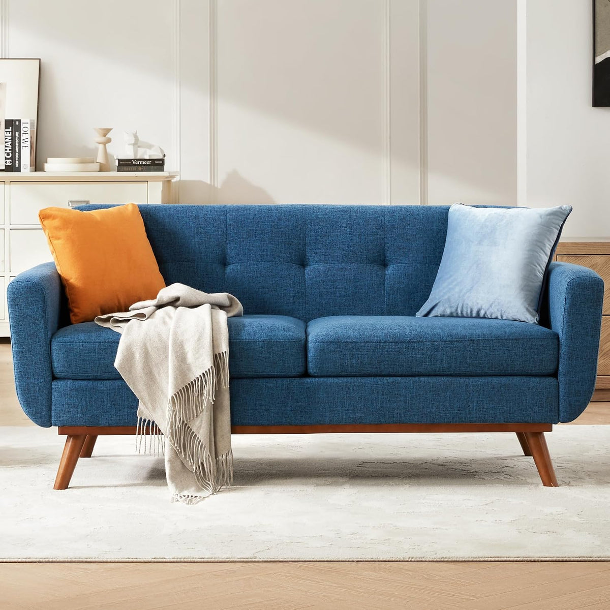 Front view of a blue mid-century loveseat with wooden legs, two pillows and a draped throw