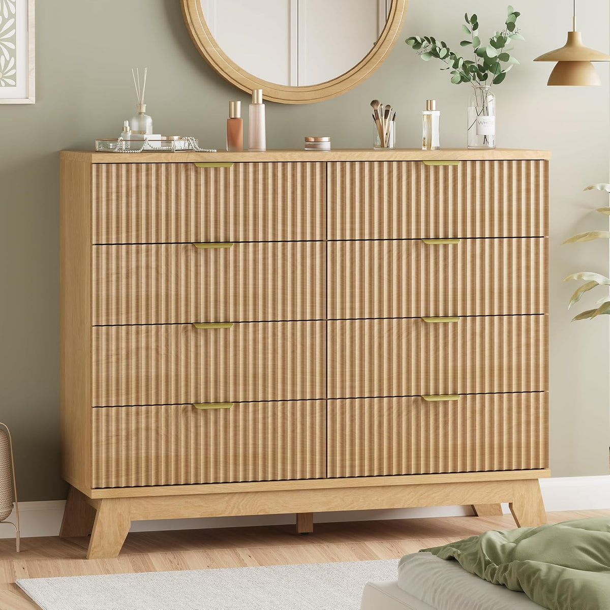 Front view of a light oak wave-panel dresser with gold handles against a green wall and round mirror.