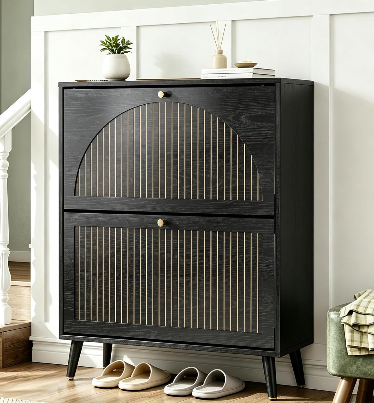 Black two-drawer shoe cabinet with gold-accented vertical grooves styled on a stair landing