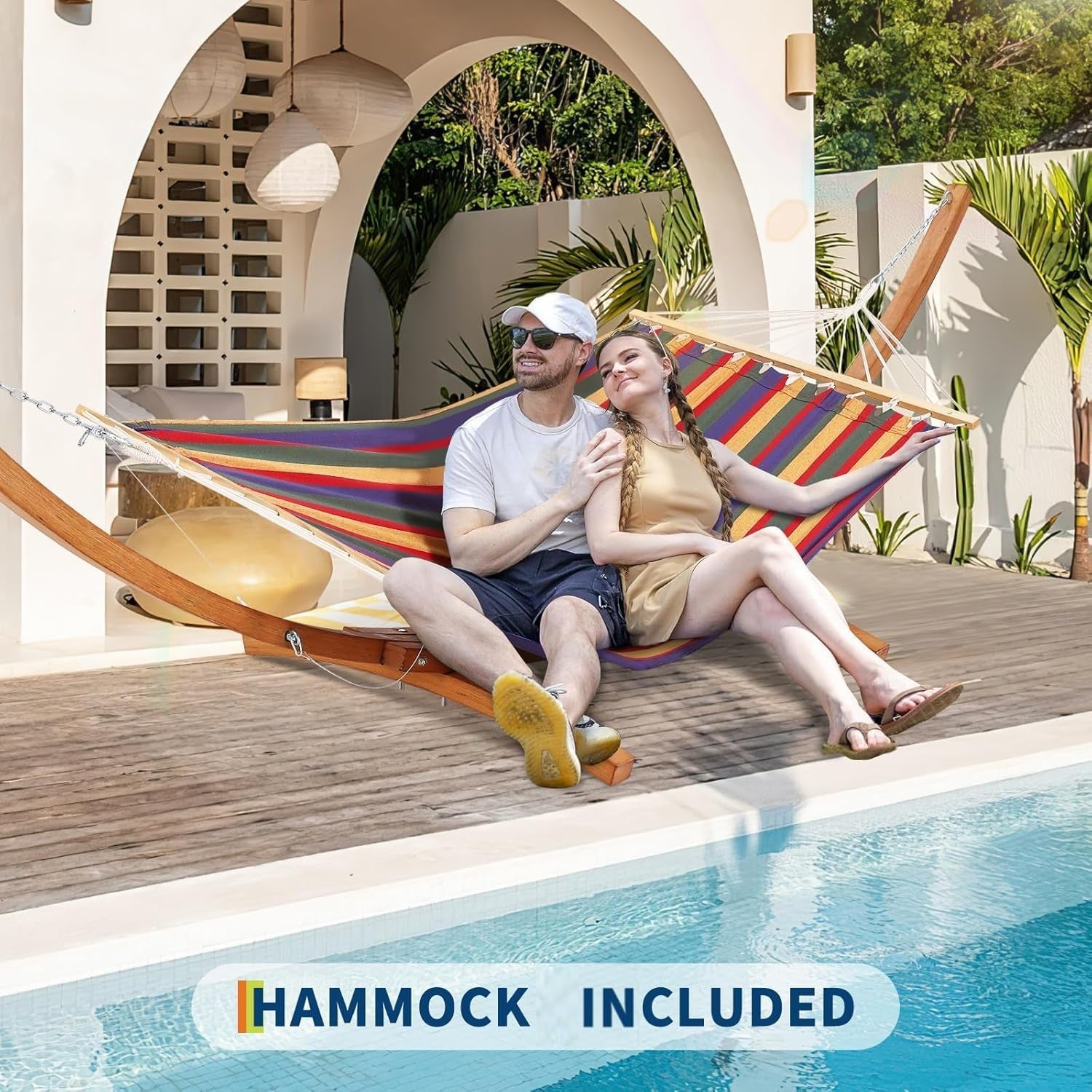 Couple reclining together on a striped hammock hung from a curved wooden stand beside a pool