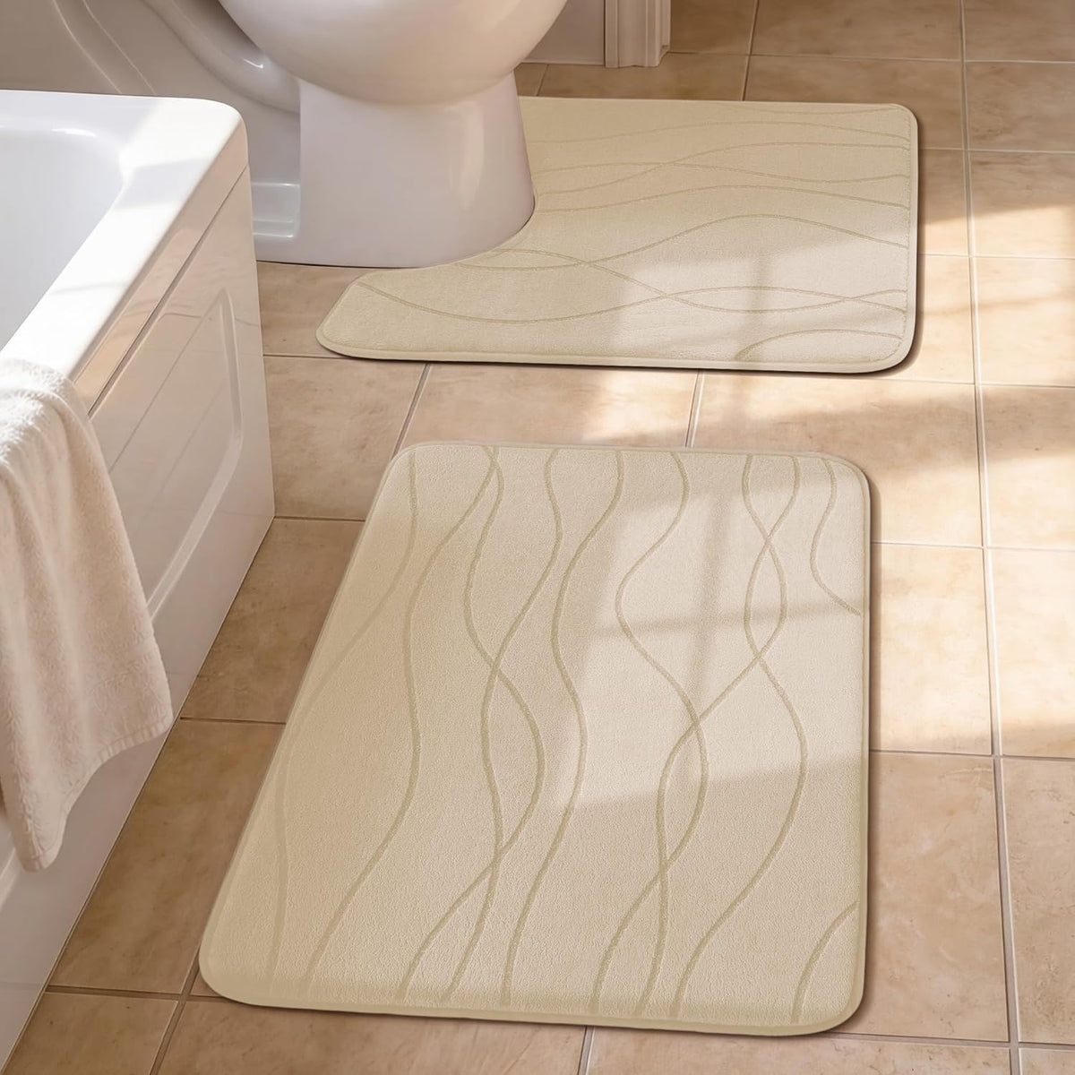 Beige rectangular bath mats with subtle wavy line pattern near a bathtub and toilet on tan tiles.