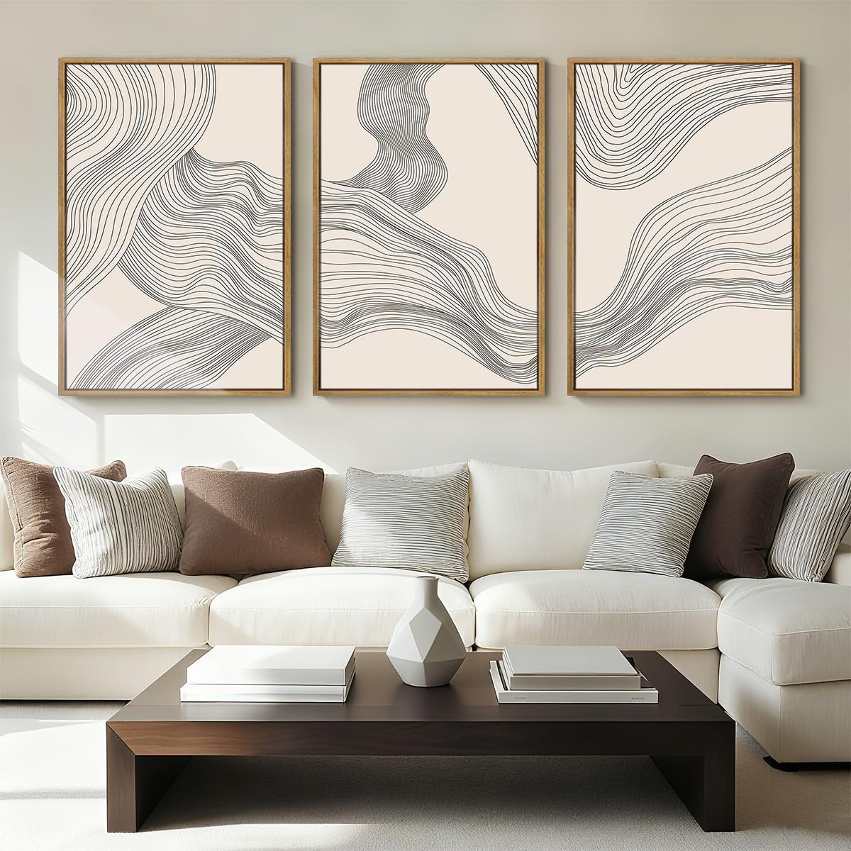 Three framed abstract linear prints above a light sofa and low dark wood coffee table in a bright living room.