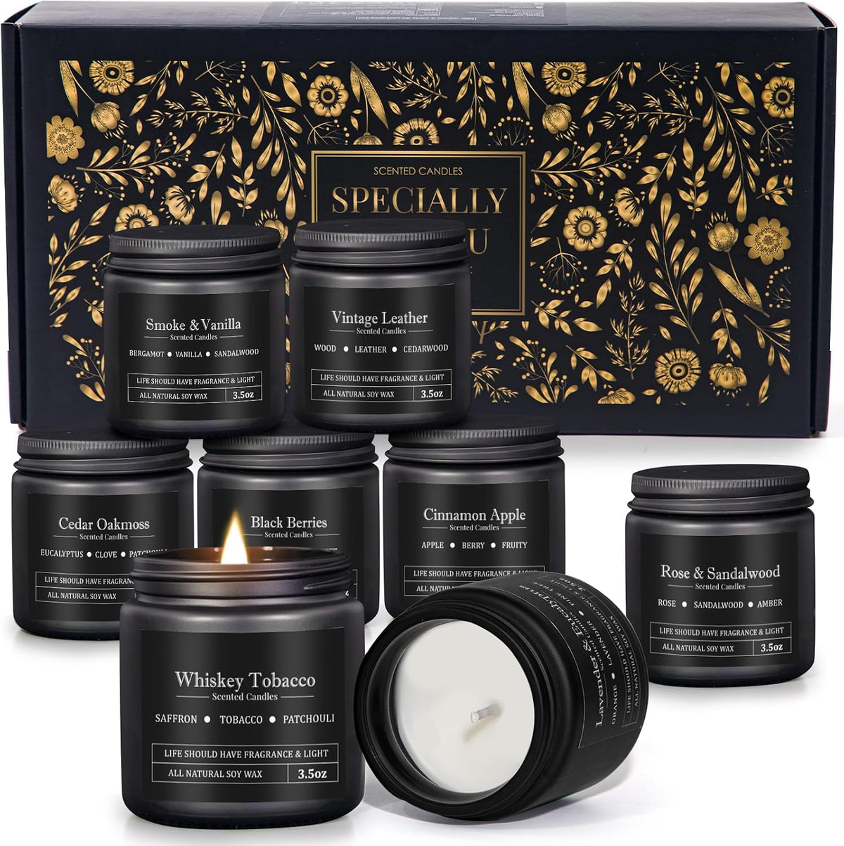 Several matte black candle jars arranged in front of a decorative black-and-gold gift box, one jar lit and one tipped to