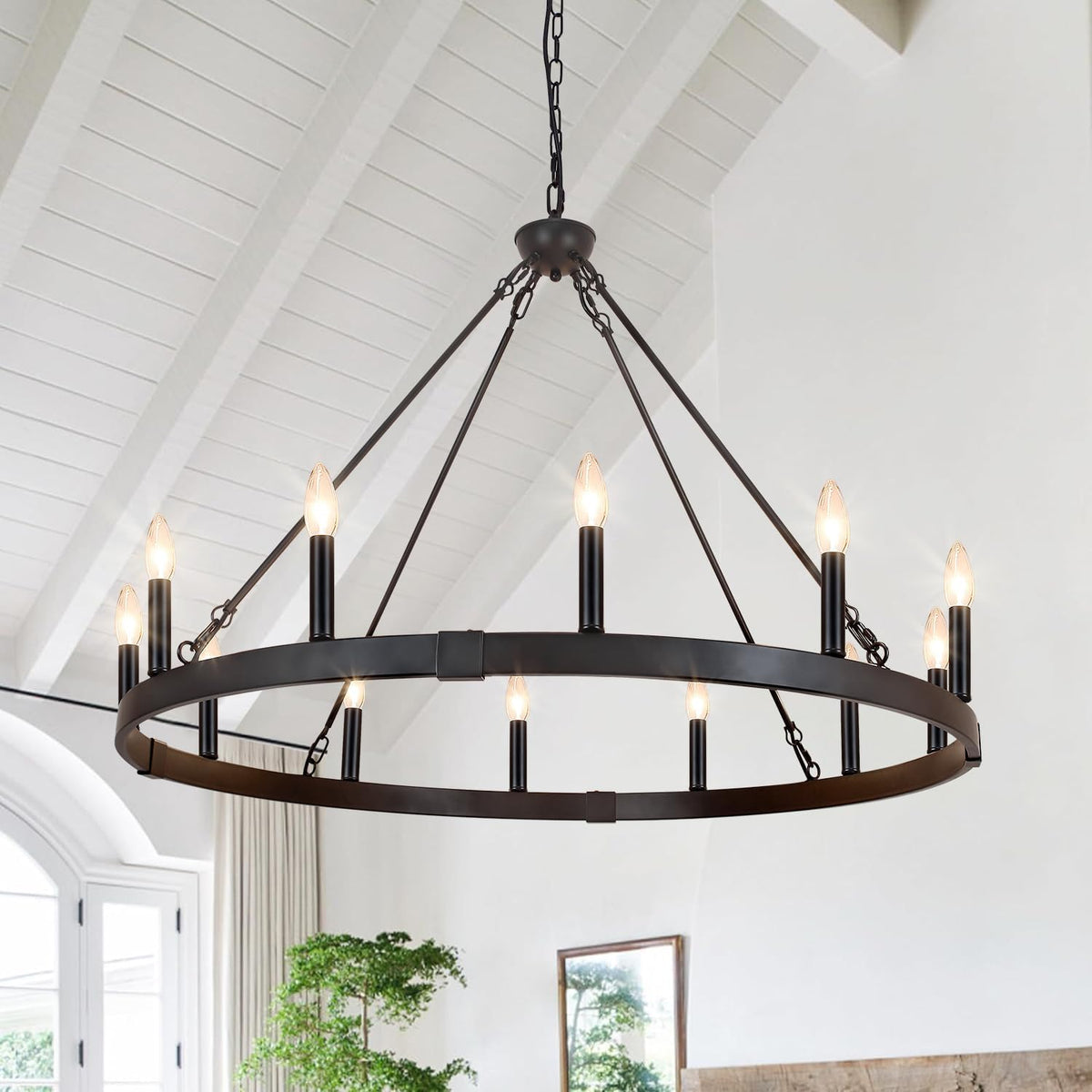 Dark metal ring chandelier hanging from a vaulted white-planked ceiling in a bright living space