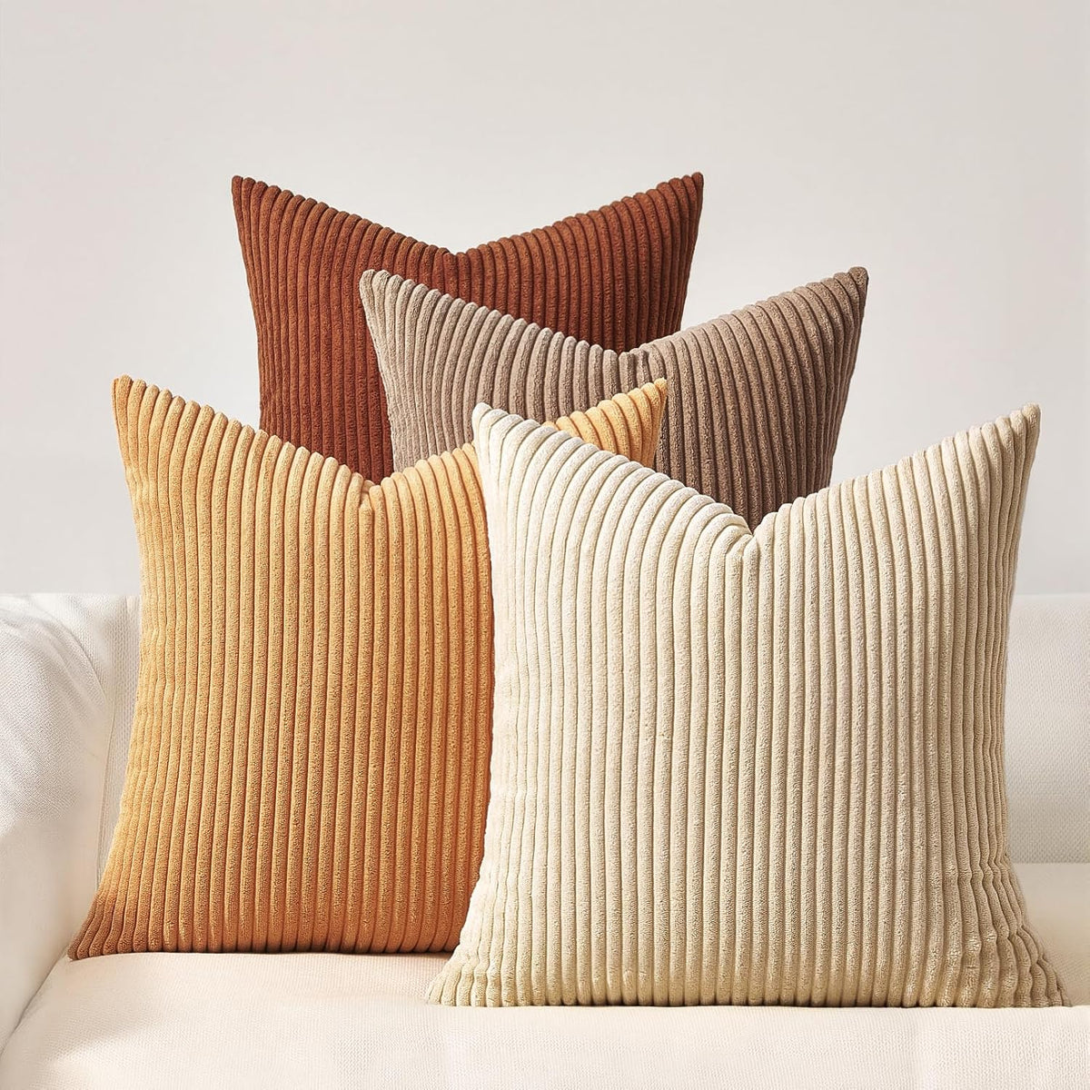 Four corduroy ribbed square pillows in warm tones arranged on a light sofa