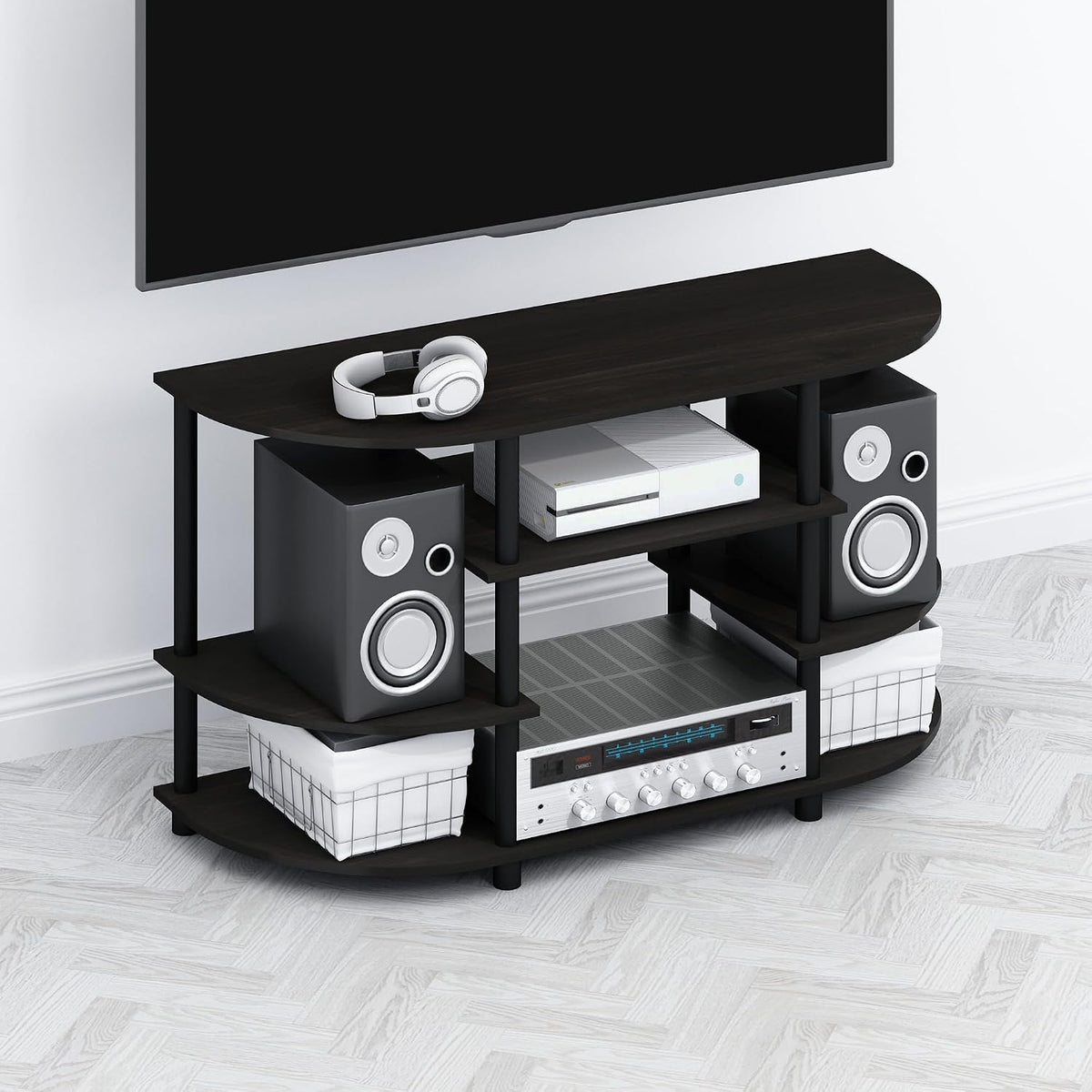 Low curved TV stand in dark finish holding speakers, a receiver and baskets beneath a mounted TV.