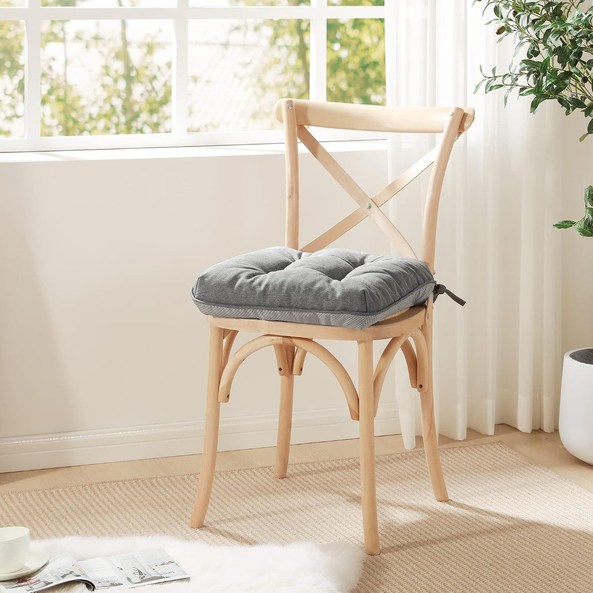 Wooden dining chair with a gray tufted cushion tied to the back, near a bright window