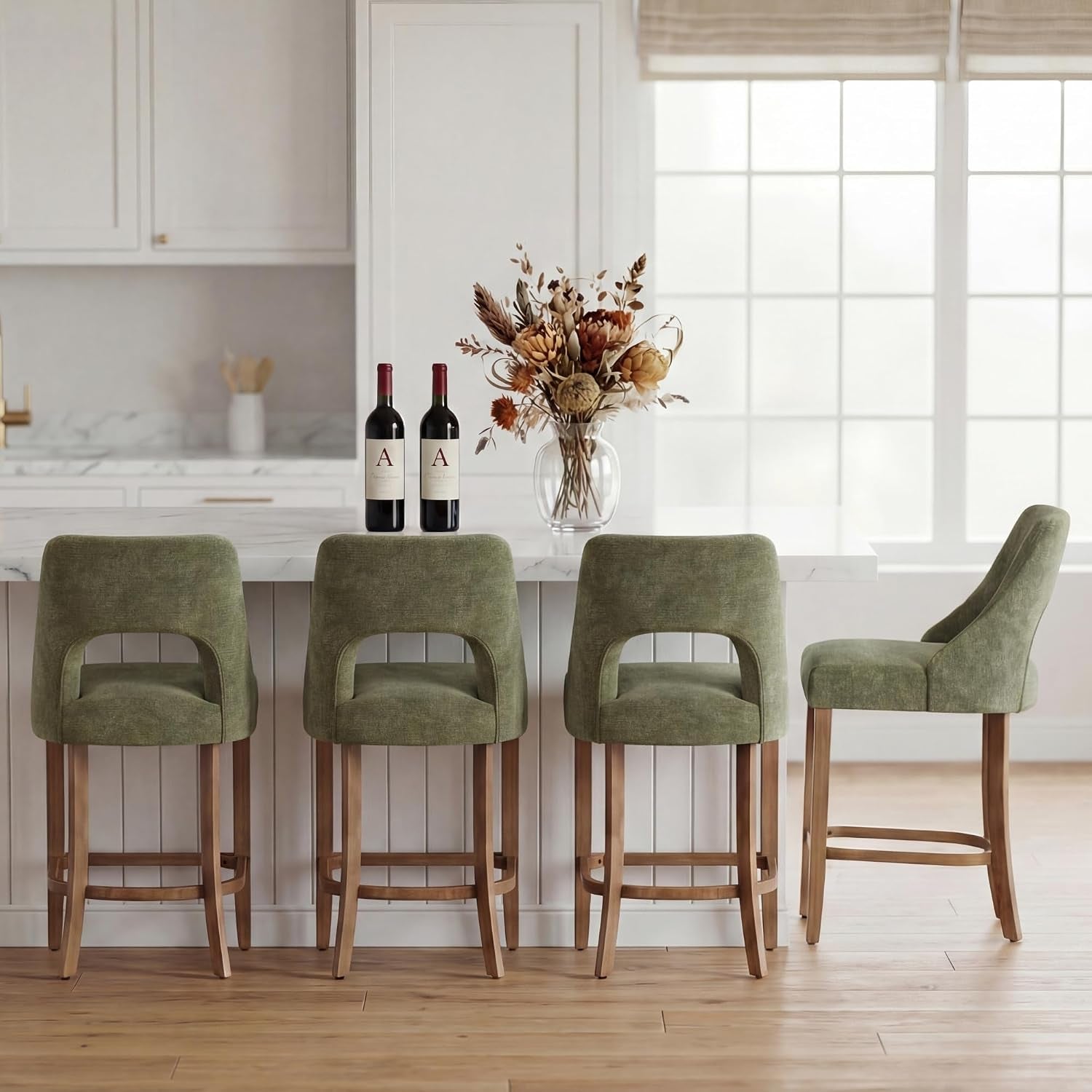 Four green upholstered counter stools with wood legs arranged at a kitchen island, one turned sideways