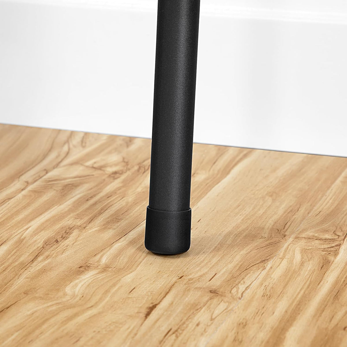 Tight detail of a single black metal leg with protective black rubber cap on a wood floor