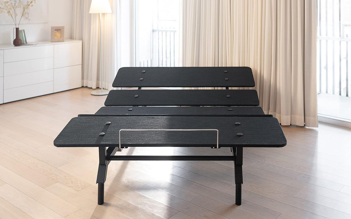 Black adjustable bed base set upright in a bright bedroom with mattress retainer bar visible at foot.