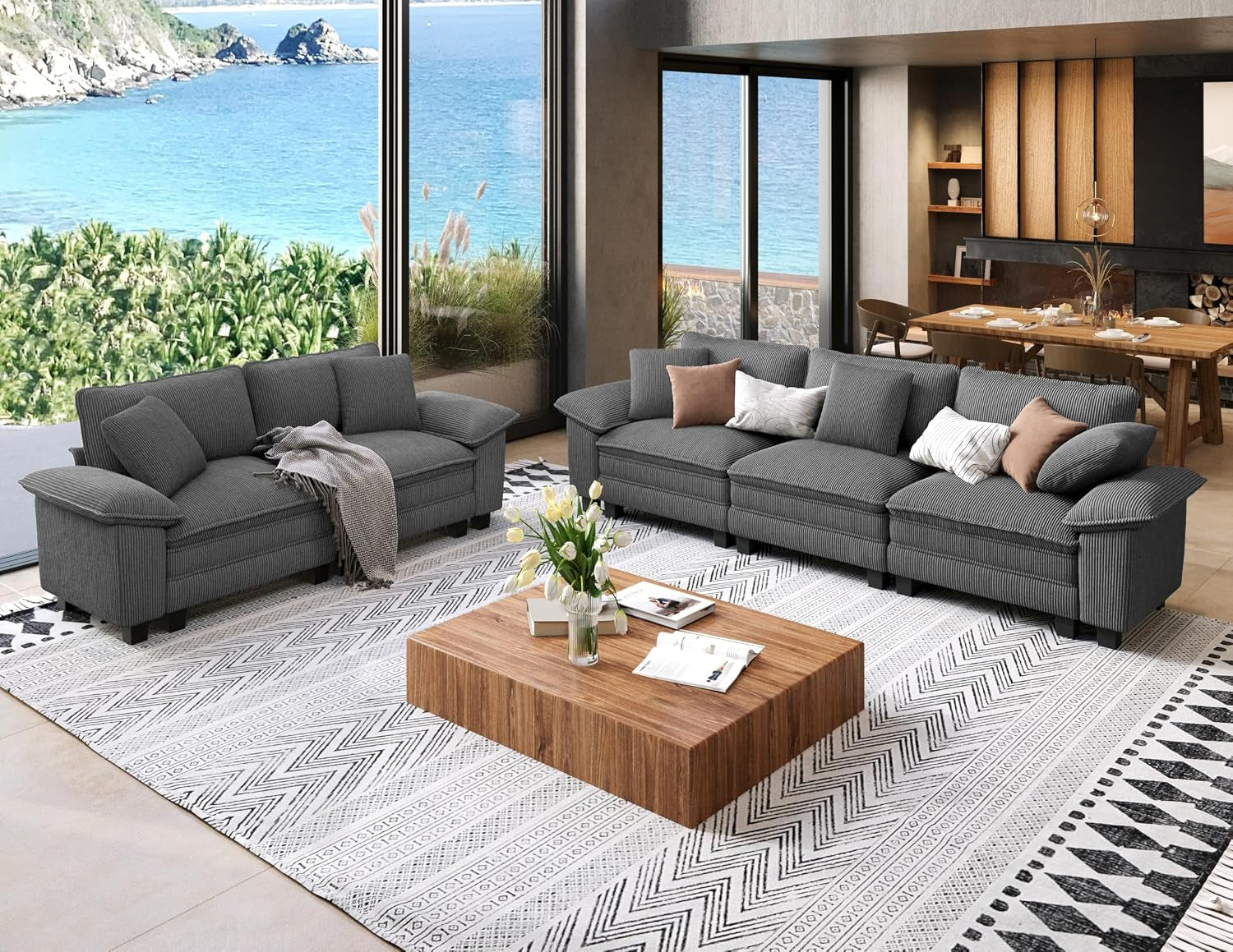 Dark charcoal three-seat sofa and loveseat arranged around a low wooden coffee table by ocean-view windows