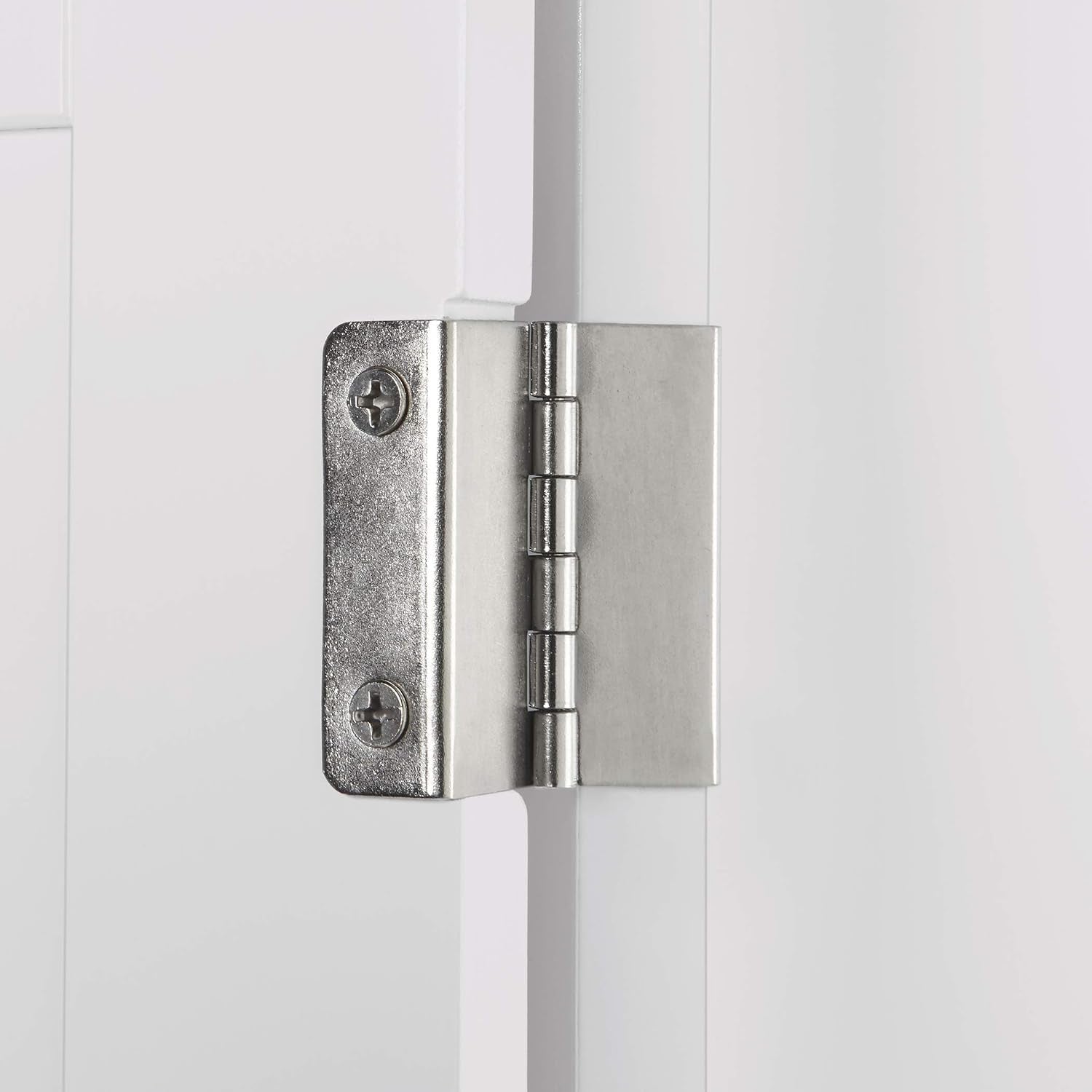 Close-up of a silver hinge attached to the edge of the white cabinet door.