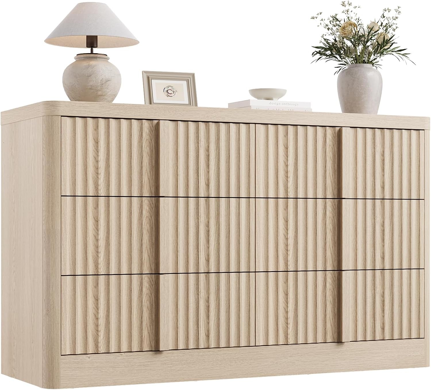 Six-drawer dresser with vertical fluted drawer fronts in a light oak finish, decorative lamp and vase on top.